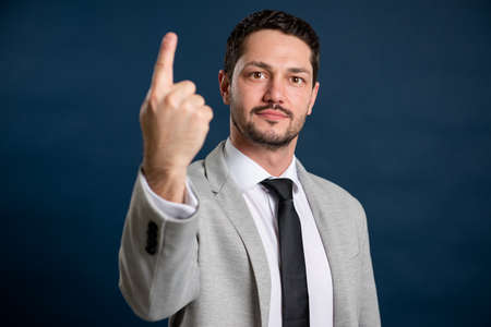 Portrait of business young handsome male showing number one gesture on blue backgroundの写真素材