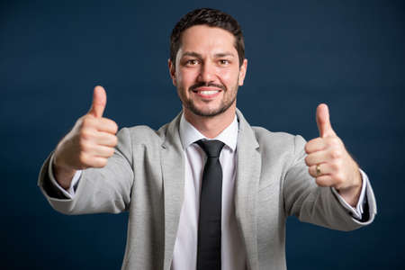 Portrait of business young handsome male showing thumb up gesture on blue backgroundの写真素材