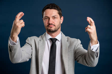 Portrait of business young handsome male showing fingers crossed gesture on blue backgroundの写真素材