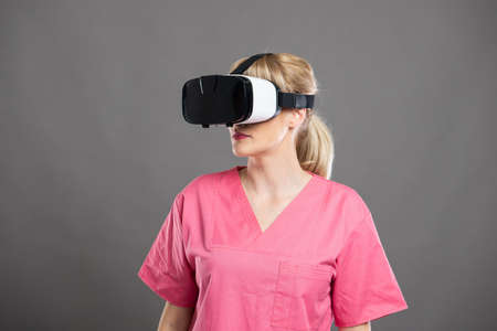 Portrait of attractive female nurse wearing virtual reality goggles on gray background