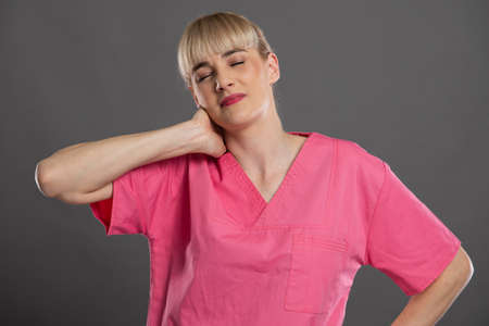 Portrait of young attractive female nurse holding neck like hurting on gray background