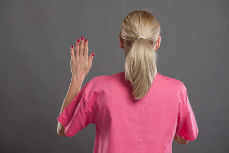 Back view of young attractive female nurse taking oath on gray background