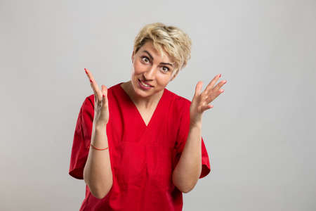 Portrait of young attractive female nurse making explaining gesture on grey background with copy space advertising areaの写真素材