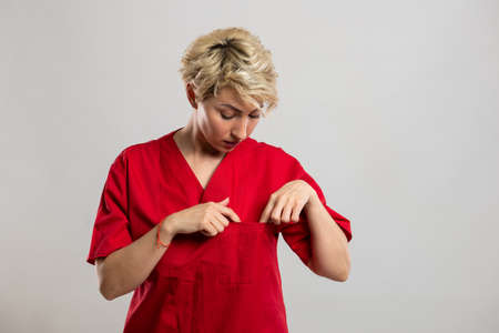 Portrait of young attractive female nurse checking pocket on grey background with copy space advertising areaの写真素材