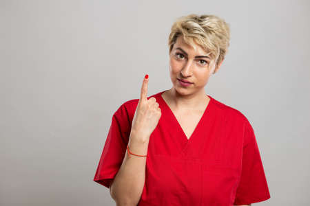 Portrait of young attractive female nurse showing number one on grey background with copy space advertising areaの写真素材