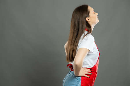 Portrait of young female supermarket employee holding empty pockets on gray background with copy...