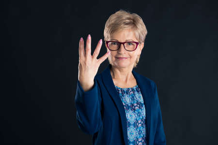 Older secretary showing number four on dark backgroundの写真素材
