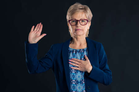 Older secretary swearing in and wearing a blue jacket with magenta glassesの写真素材
