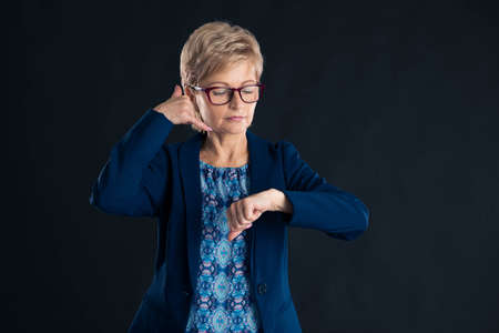 Senior secretary making call me on time gesture on a dark background