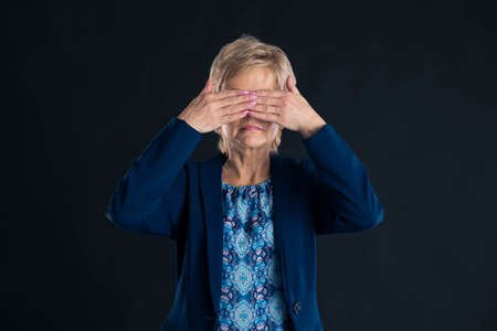 Senior businesswoman having her hands up to her eyes so she does not see on a dark backgroundの写真素材