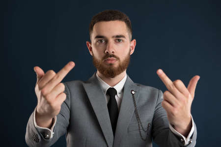 Serious young businessman showing double fuck you wearing a grey suit and a black tieの写真素材
