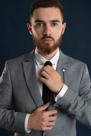 Portrait of a young businessman fixing his black tie wearing a grey suitの写真素材