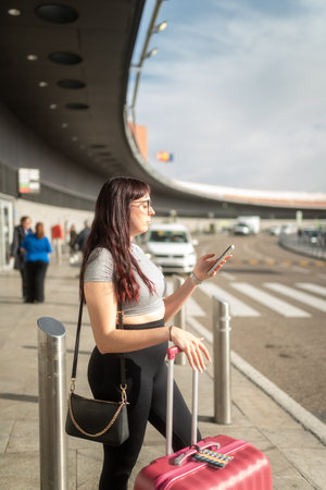 Young woman using smartphone while waiting for ride-sharing at airportの写真素材