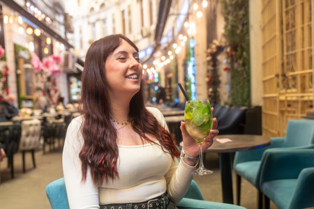 Smiling woman enjoying refreshing mojito cocktail outdoors at christmas time