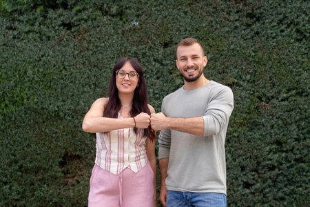 Young couple fist bumping celebrating success in front of hedge