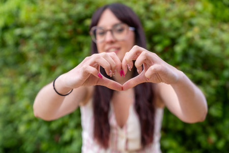 Young woman making heart shape with hands outdoors, showing love and happinessの写真素材