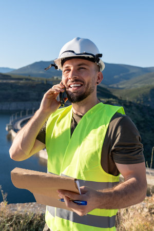 Smiling engineer talking on phone and taking notes near damの写真素材