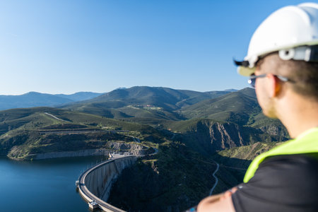 Engineer observing dam and reservoir in mountain valley