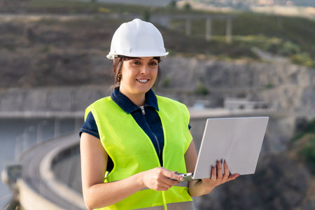 Female engineer using laptop managing infrastructure near damの写真素材