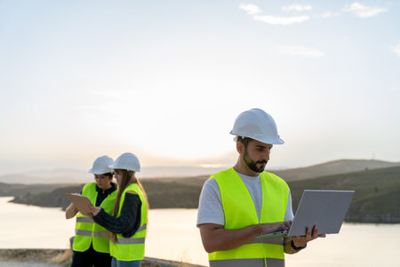 Engineers working with laptop and tablet near a lake at sunset promoting technical careersの写真素材