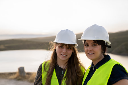 Female engineers wearing hard hats and safety vest smiling at construction site