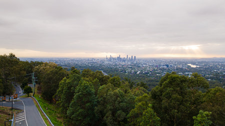Brisbane skyline emerging from lush forest at sunrise under cloudy skyの写真素材