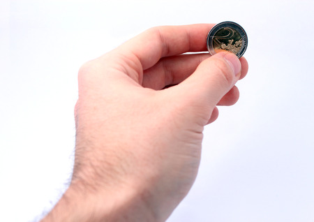 Male hand giving 2 euro coin isolated on white background in studio, symbol for donation, purchase, deal, exchange.の写真素材