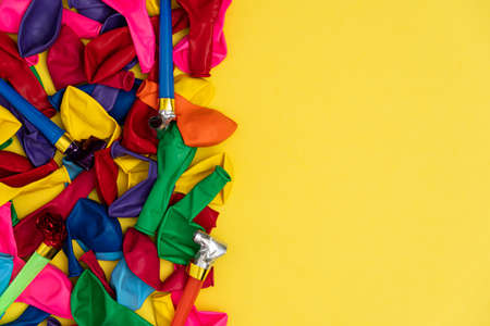 Deflated balloons and whistles, with copy space. Mix of colored balloons and party whistles on yellow background, with right copy space, top view. Perfect template for social media event and birthday invitations.の写真素材