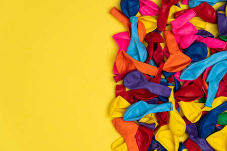 Close up view of colored deflated balloons. Top view of colored balloons on yellow background, with left copy space, flat lay. Great for birthday store sales and promotions.の写真素材
