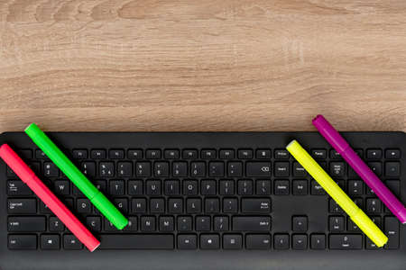 Black keyboard on wooden desk with markersの写真素材