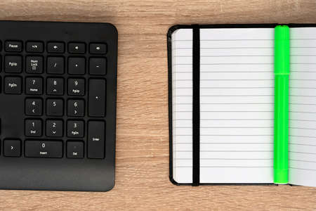 Keyboard with green pen on open notepadの写真素材