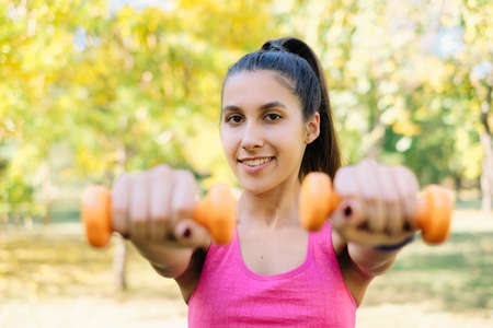 Girl doing arm exercise with dumbbells in the nature