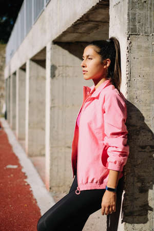 Brunette girl with pink jacket leaning at column