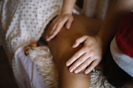 Close-up of masseuse hands massaging female shoulder. Cropped masseuse massaging woman's shoulder on massage bed with Christmas balls, with copyspace, close-up. Image can be used in websites, advertising, blogs and articles.の写真素材