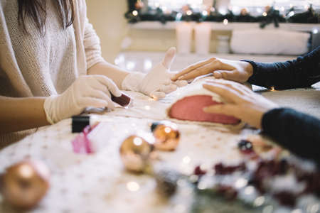 Cropped manicurist holding red nail polish, ready to work. Female manicurist holding dark red nail polish and woman's hand on table at nail salon decorated for Christmas, with copyspace, close-up. Image can be used in websites, advertising, blogs and articles.の写真素材