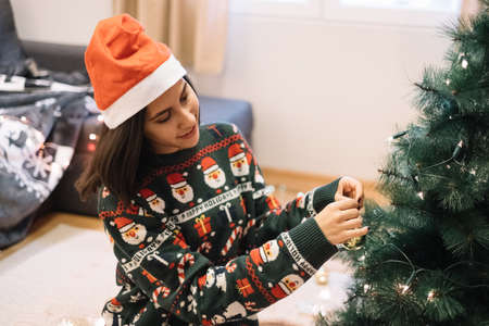 Girl with Santa hat decorating tree with Christmas toys