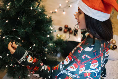 Side view of girl with Santa hat wrapping tree with lights onの写真素材