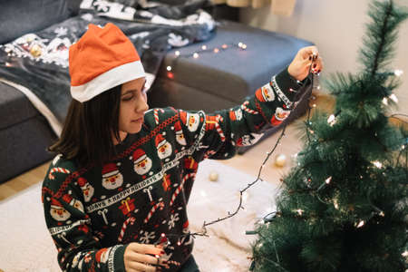 Pretty girl with Santa hat puting lights to treeの写真素材