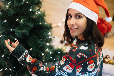 Girl looking at camera while wrapping tree with lightsの写真素材