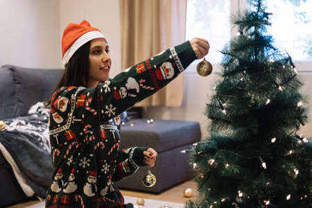 Smiling girl with Santa hat putting golden ball to the treeの写真素材