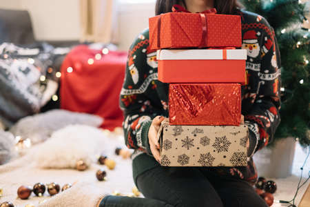 Cropped woman holding wrapped presents while sitting on floor