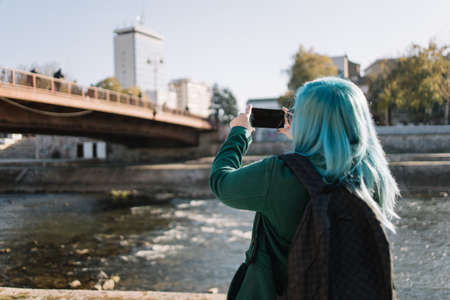 Close-up of woman taking photo with phone. Back of woman with blue hair taking photo with her...
