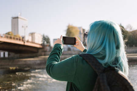 Woman making selfie while standing side river. Female traveler looking at her phone and making selfie while standing near city river, with copyspace. Photo can be use in websites, blogs, adverts, leaflet, cards.の写真素材