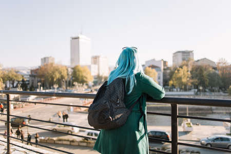 Young tourist woman on vacation with a map. Back view of a girl with blue hair and green coat on fence looking city map, with copyspace, close-up. Perfect for magazines, brochures, flyers and posters.の写真素材