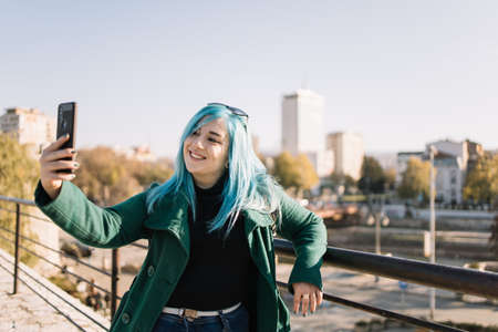 Woman taking selfie while leaning on fence with city view