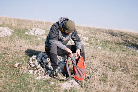 Hiker man sitting on a rock and looking into his backpack