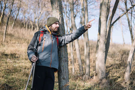 Tourist man holding poles and pointing for direction in mountainの写真素材