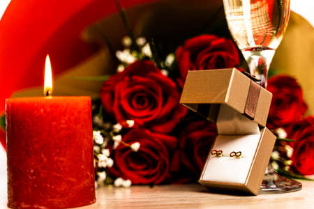 Close-up of burning red candle and earrings in gift box. Romantic surprise with burning red candle,...