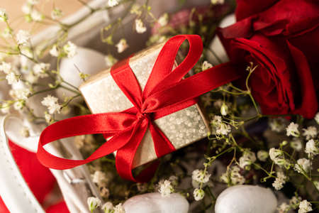 Close-up of wrapped Valentines day gift with gypsophila. Golden gift box with red ribbon surrounded...