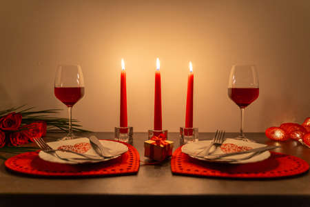 Romantic table with candles and wine for Valentines day. Night view of burning candles on table with red wine glasses, gift and plates.の写真素材
